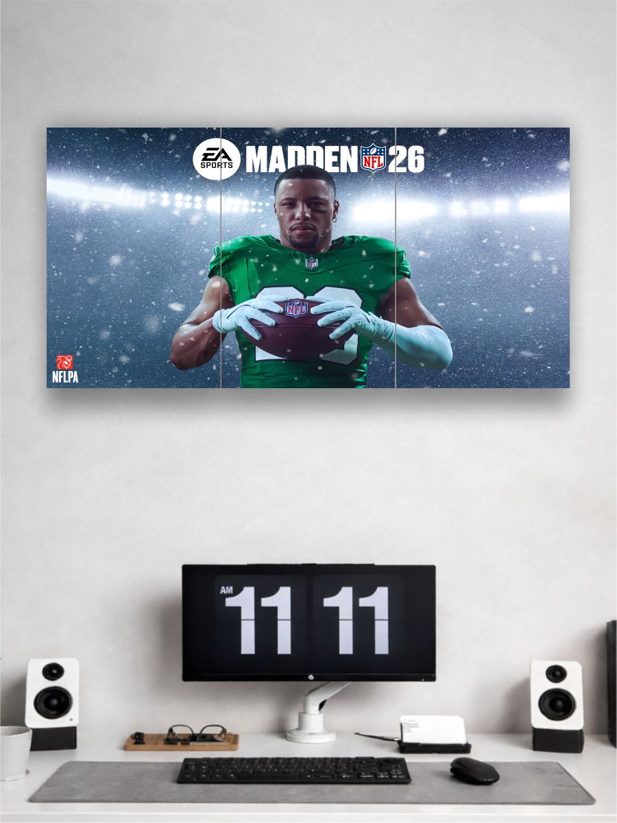 Wall-mounted TV displaying 'Madden NFL 26' with a football player holding a ball, below a computer setup on a desk.